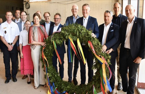 Gro&szlig;er Richtkranz f&uuml;r ein gro&szlig;es Geb&auml;ude: Ministerpr&auml;sident Gordon Schnieder (4. v. r.), OB Wolfram Leibe (5. v. r.), Landr&auml;tin Julia Gieseking (Vulkaneifel), ihre Amtskollegen Stefan Metzdorf (Trier-Saarburg), Andreas Hackethal (Bernkastel-Wittlich), Andreas Kruppert (Bitburg-Pr&uuml;m) und Miroslaw Kowalski (Birkenfeld) sowie weitere Projektbeteiligte freuen sich &uuml;ber den Baufortschritt